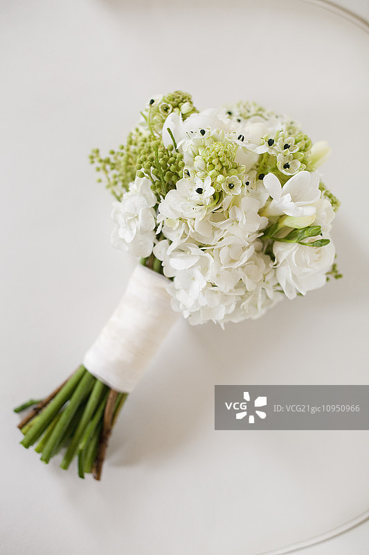 一个婚礼花束。白色的切花，绿色的种子头和叶。绿色的茎和白色的丝带。图片素材