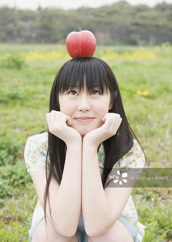 微笑的女孩把一个苹果放在她的头上图片素材