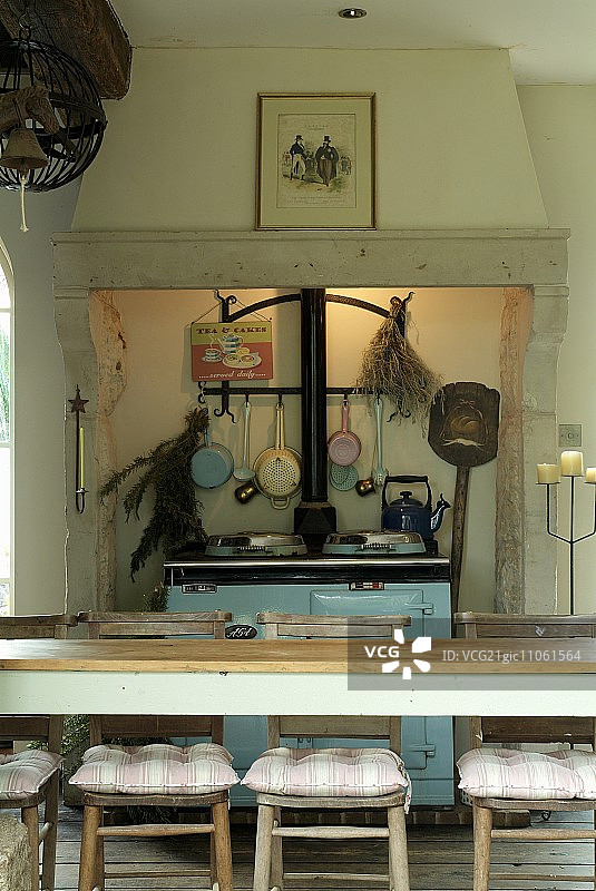 长长的餐桌和木椅，前面是怀旧的、浅蓝色的炊具，壁炉的烟囱罩上有间接照明图片素材