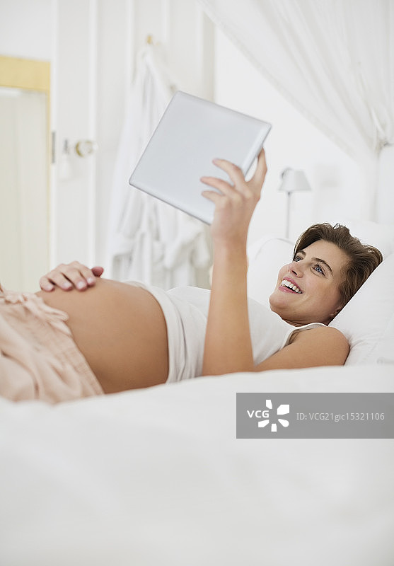孕妇在床上使用平板电脑图片素材