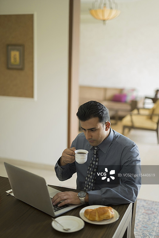 印度，商人在家里用笔记本电脑喝咖啡图片素材
