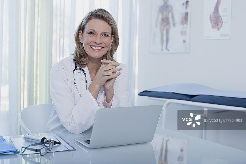 微笑的女医生坐在办公桌前，用笔记本电脑办公图片素材