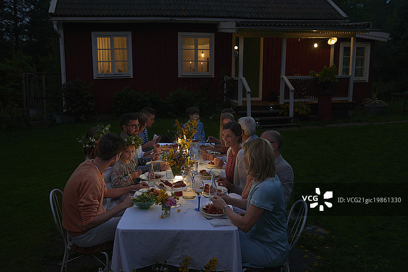 家庭享受烛光晚餐在露台桌子外面的房子在晚上图片素材