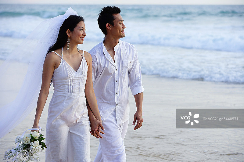 新婚夫妇走在沙滩上，手牵着手，看向别处图片素材