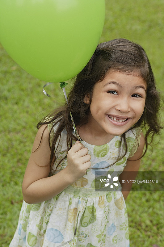 女孩拿着绿色的气球，对着镜头微笑图片素材