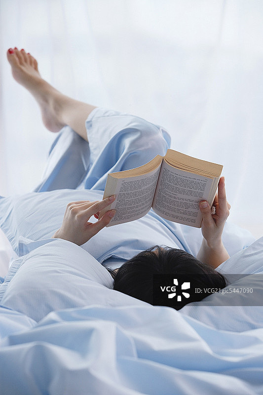 年轻女子躺在床上，正在看书图片素材
