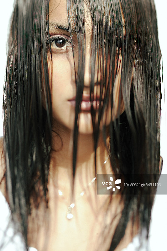 年轻女子看着镜头，湿漉漉的长发遮住了她的脸图片素材