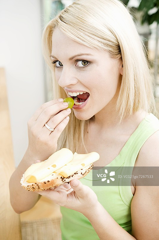 女人咬着葡萄，拿着奶酪三明治图片素材