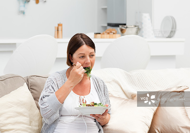 坐在沙发上吃蔬菜的孕妇图片素材