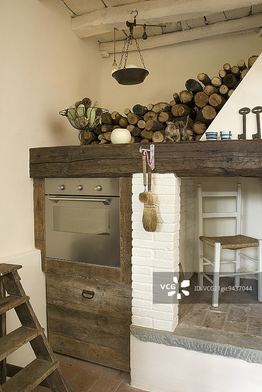 厨房的一角，一个质朴的木制橱柜里有内置的不锈钢烤箱，旁边有一个烟囱和一个存放木柴的地方图片素材