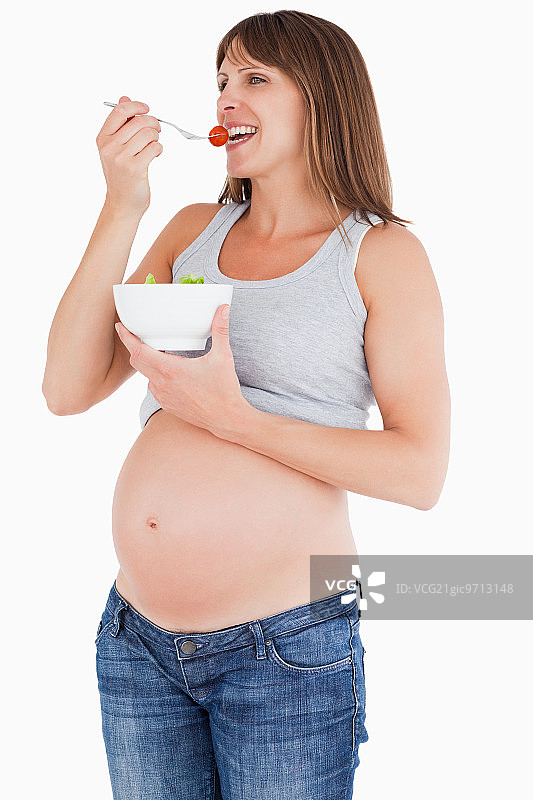 美丽的孕妇在白色背景下拿着一碗沙拉吃着樱桃番茄图片素材