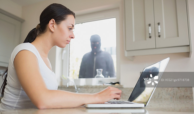 年轻女子在笔记本电脑屏幕上看到强盗的影子图片素材