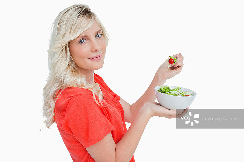 一个年轻的金发女人吃新鲜的沙拉的侧面的背景白色图片素材