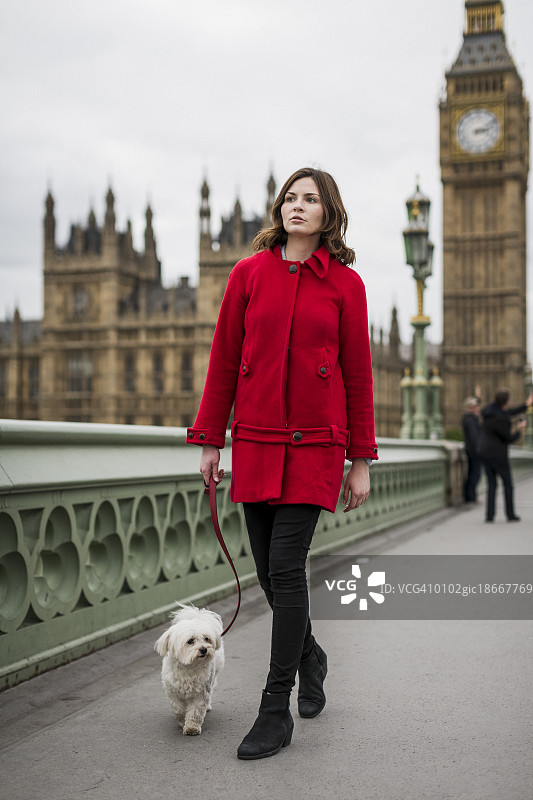 穿着红色夹克的年轻女子带着她的狗散步图片素材