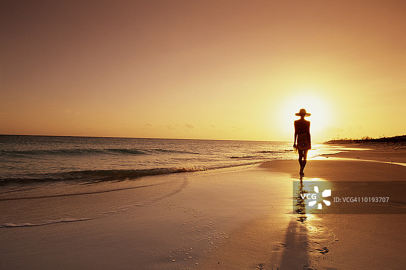 日落时分，在海滩上散步的女人图片素材
