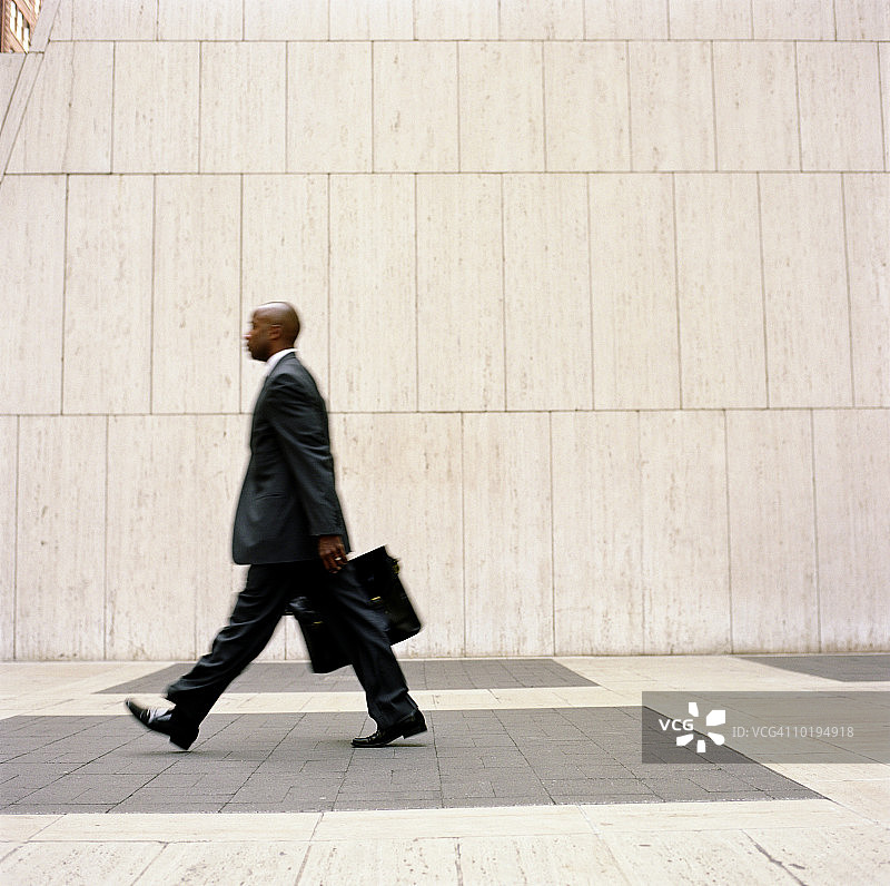 商人走在办公大楼广场上，侧面(模糊动作)图片素材