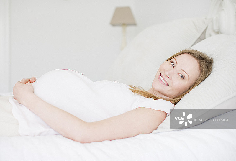 微笑的孕妇躺在床上图片素材