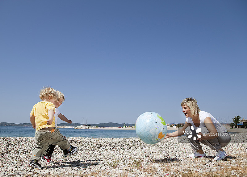母亲和双胞胎在海滩上玩球图片素材