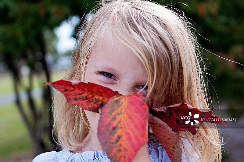 女孩把她的微笑藏在秋叶后面图片素材