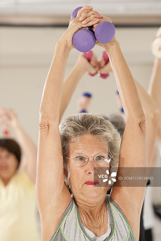 一个年长妇女在健身俱乐部用哑铃锻炼的特写图片素材