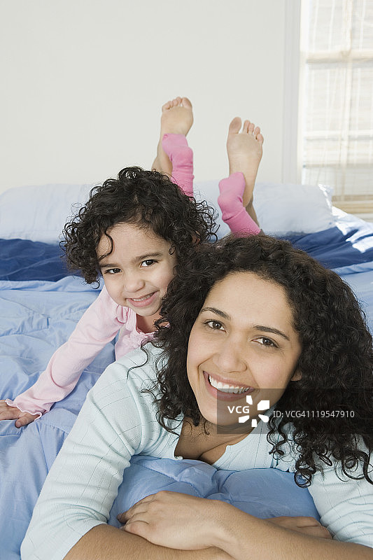 一个西班牙妇女和她的女儿在床上微笑的肖像图片素材