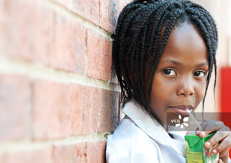 南非豪登省约翰内斯堡，女孩在学校外面用吸管喝果汁的肖像图片素材