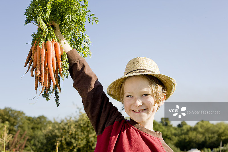 男孩戴着草帽，拿着一串胡萝卜，画像图片素材