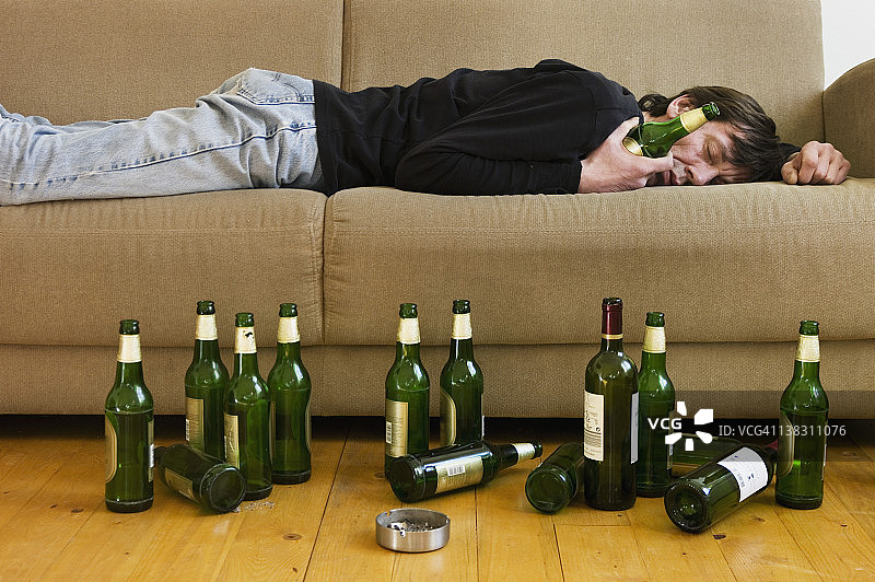 德国，黑森，法兰克福，一个醉汉躺在沙发上，手里拿着空啤酒瓶图片素材