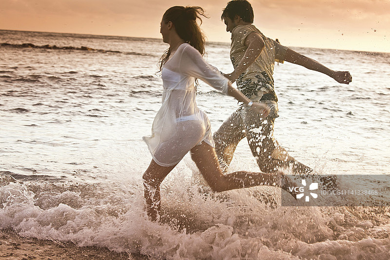 沙滩上的情侣在海浪中奔跑图片素材