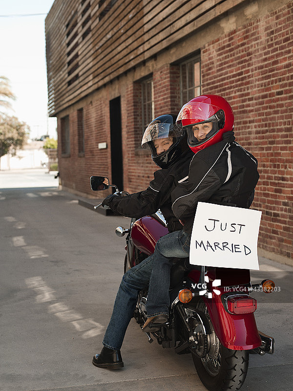 一对白人夫妇骑着摩托车，脸上挂着"新婚"的标志图片素材