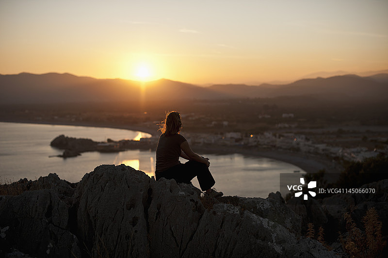 一个人的剪影坐在山顶上看日落，罗德，希腊图片素材