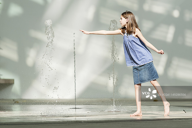 女孩试图从公共喷泉中获得垂直的喷水装置图片素材