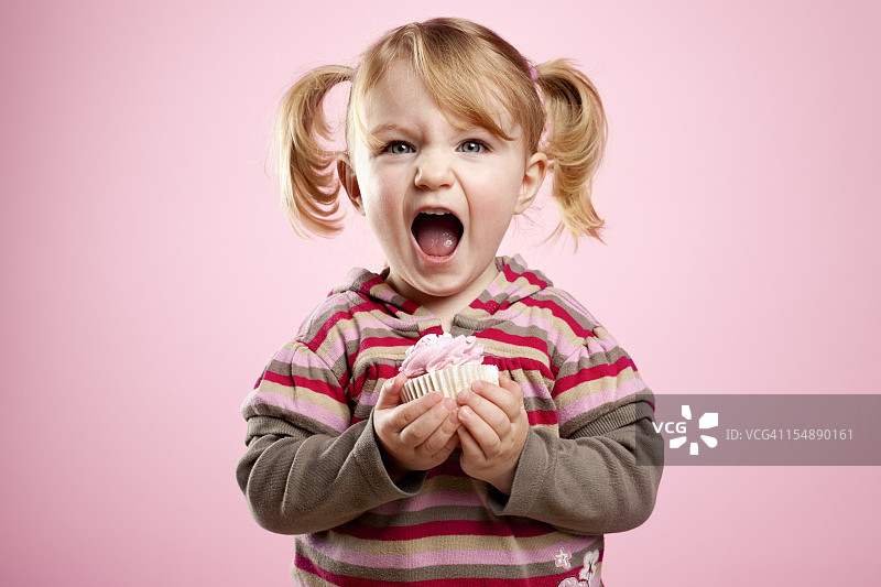 可爱的小女孩，脏兮兮的笑着，手里拿着一个粉红色的松饼。图片素材
