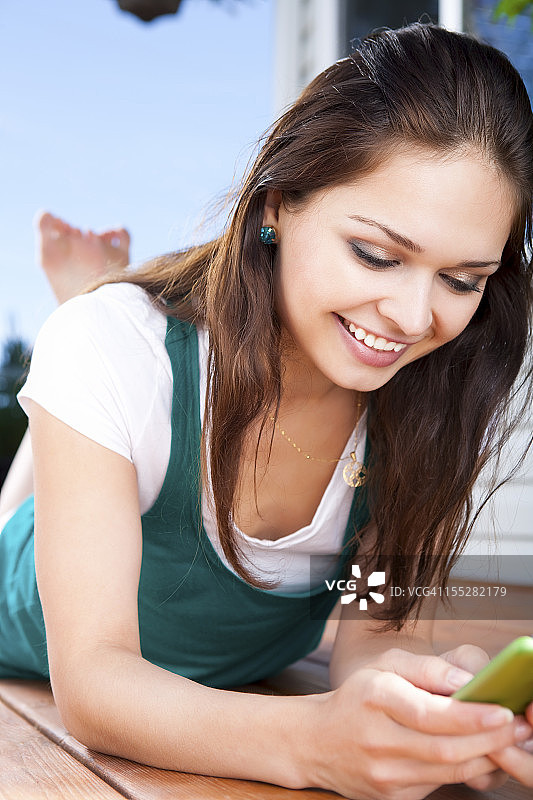 一个微笑的年轻女子在后院用手机发短信图片素材