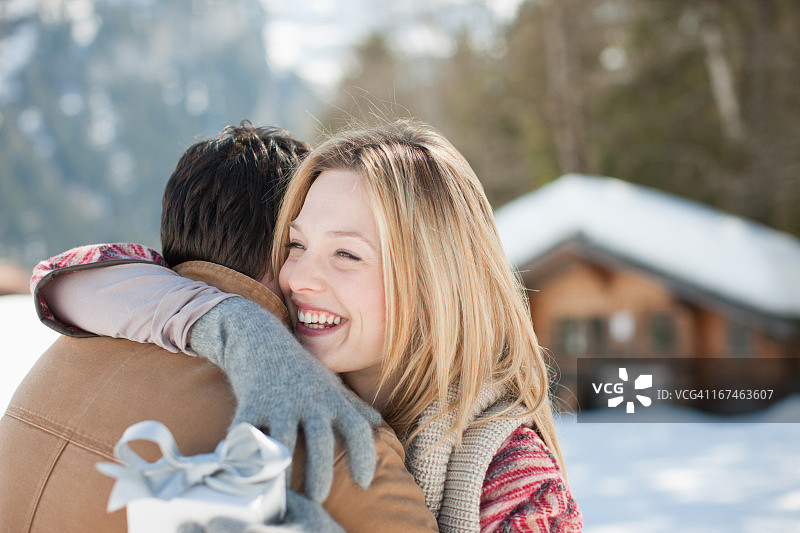 微笑的女人拿着圣诞礼物，拥抱在雪地里的男人图片素材