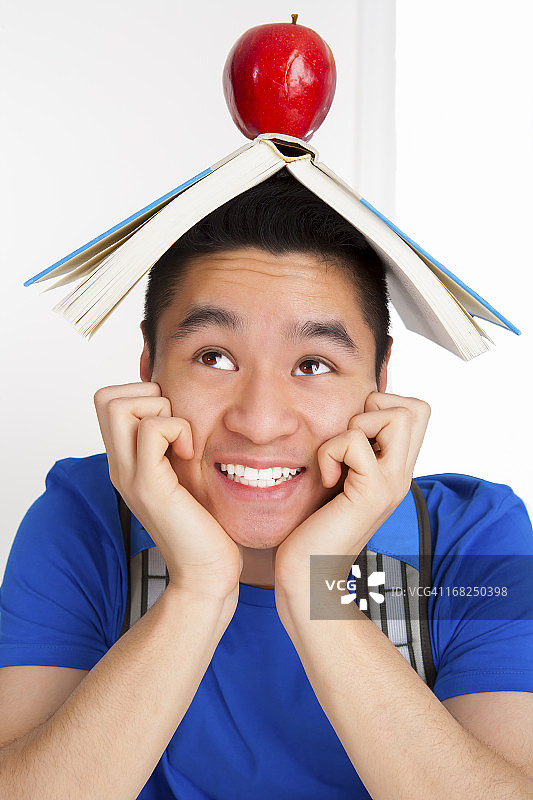 面带微笑的男学生，头上顶着书和苹果图片素材