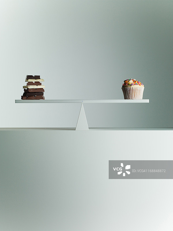 巧克力棒和纸杯蛋糕平衡在跷跷板上图片素材