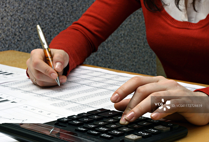 红色的女人用钢笔和计算器处理财务文件图片素材