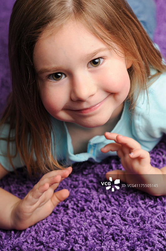 近距离的微笑小女孩躺在紫色的地毯上图片素材