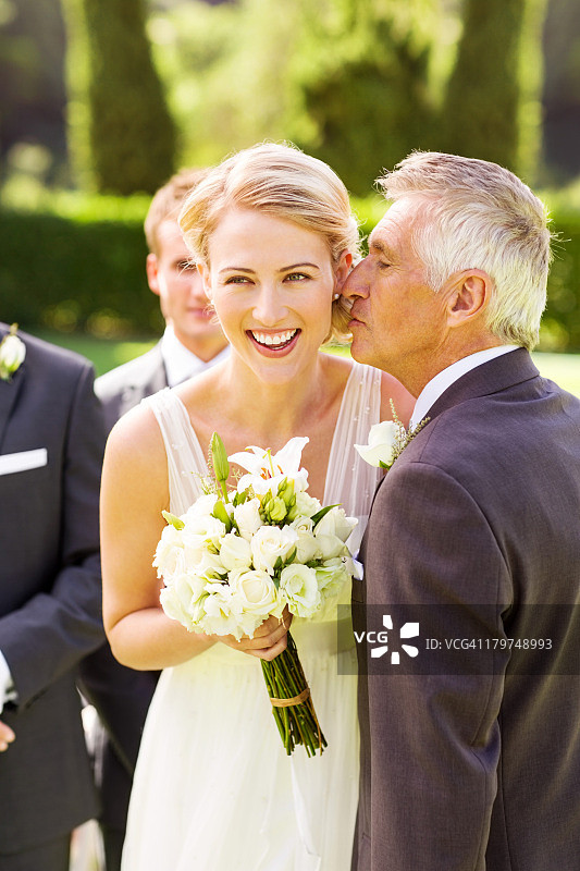当父亲亲吻她的脸颊时，新娘看向别处图片素材