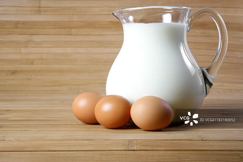 木桌上有一罐牛奶，旁边放着三个棕色的鸡蛋图片素材