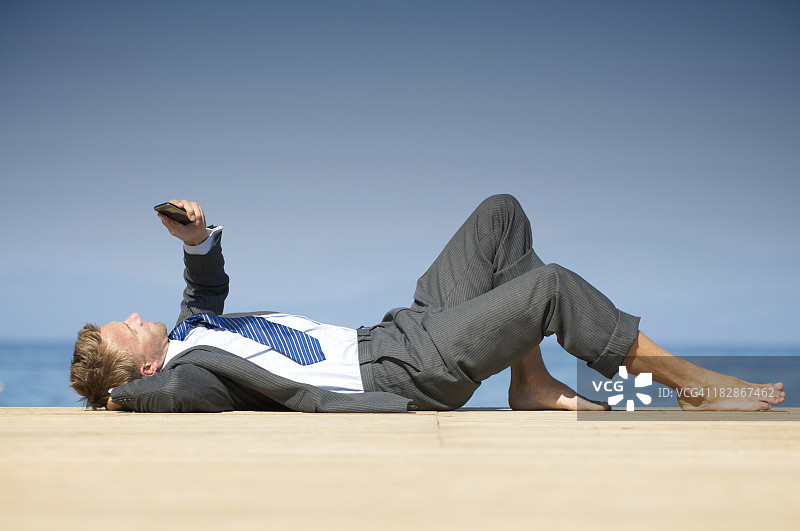 赤脚商人躺在阳光码头放松与电话图片素材