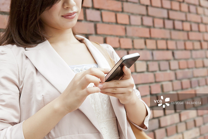 一名年轻女子在用智能手机，倚着砖墙图片素材