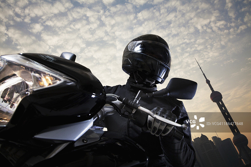白天，年轻人骑着摩托车，背景是天空和建筑物的外观图片素材