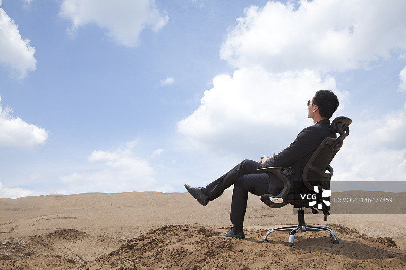 一个年轻的商人坐在沙漠中的办公椅上图片素材