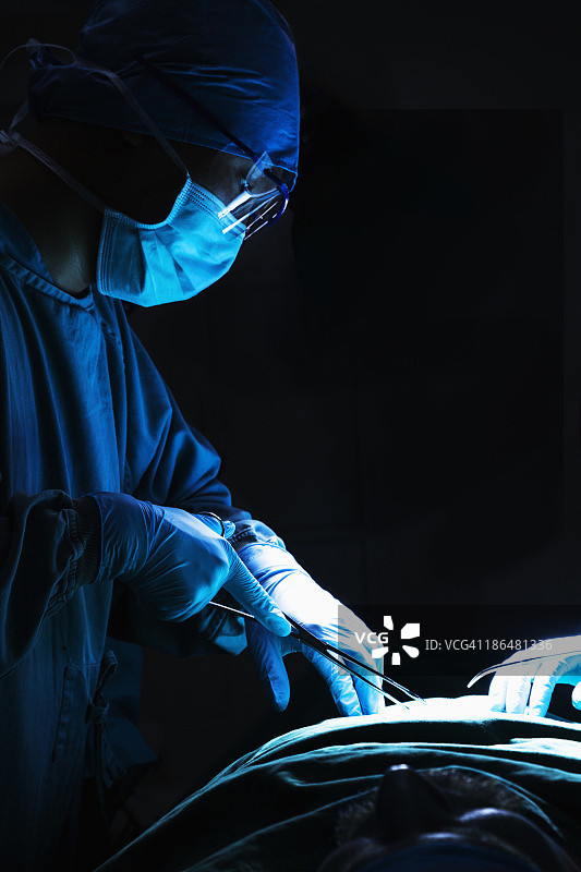 外科医生低头工作，手持手术器械，病人躺在手术台上图片素材