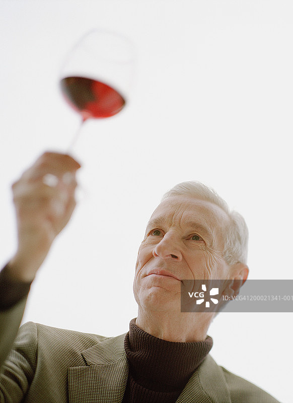 成熟的男人拿着一杯红酒对着灯光图片素材