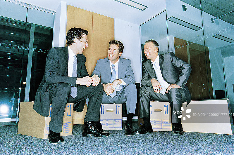三个商人坐在纸箱上大笑图片素材