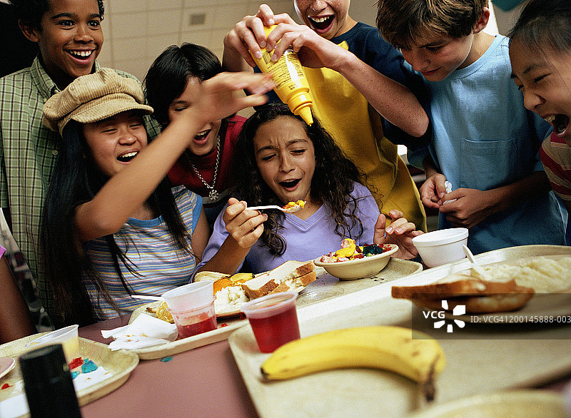 一群孩子(12-14岁)围着桌子，小男孩往食物里倒芥末图片素材