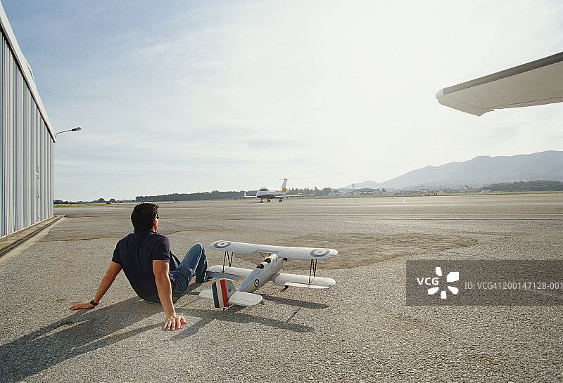 男人坐在机场的停机坪上和玩具飞机，后视镜图片素材
